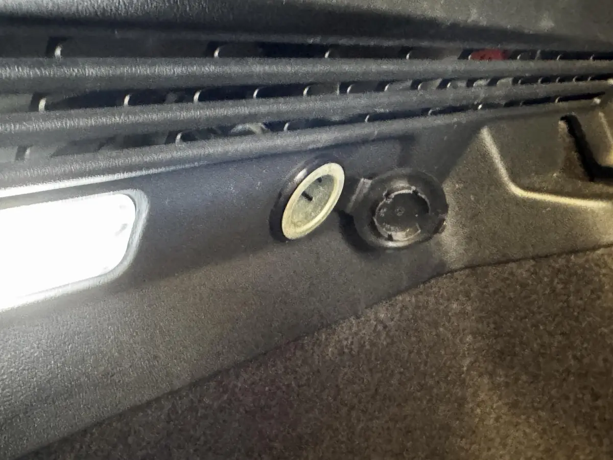 Détail intérieur du coffre du Volkswagen ID.4 77 kWh blanc montrant la prise 12V et l’éclairage d’ambiance.