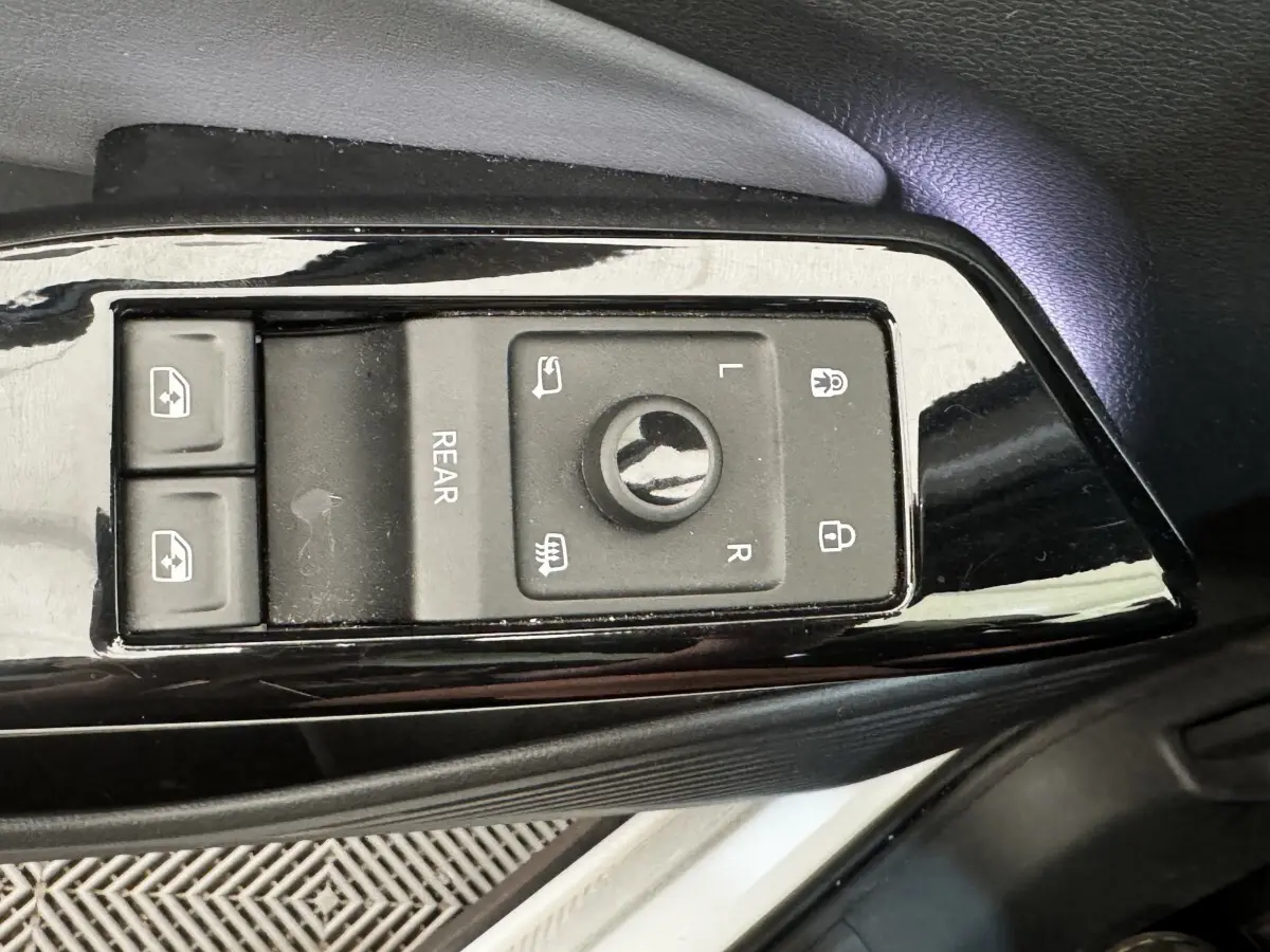 Gros plan sur les commandes noires de réglage des rétroviseurs et des vitres côté conducteur d’un Volkswagen ID.4 blanc.