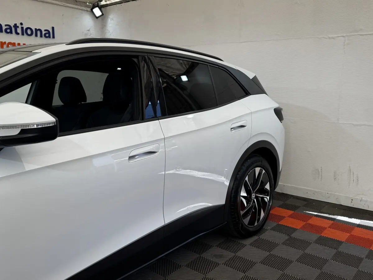 Vue côté droit arrière du Volkswagen ID.4 blanc avec jantes noires et vitres teintées en intérieur showroom.