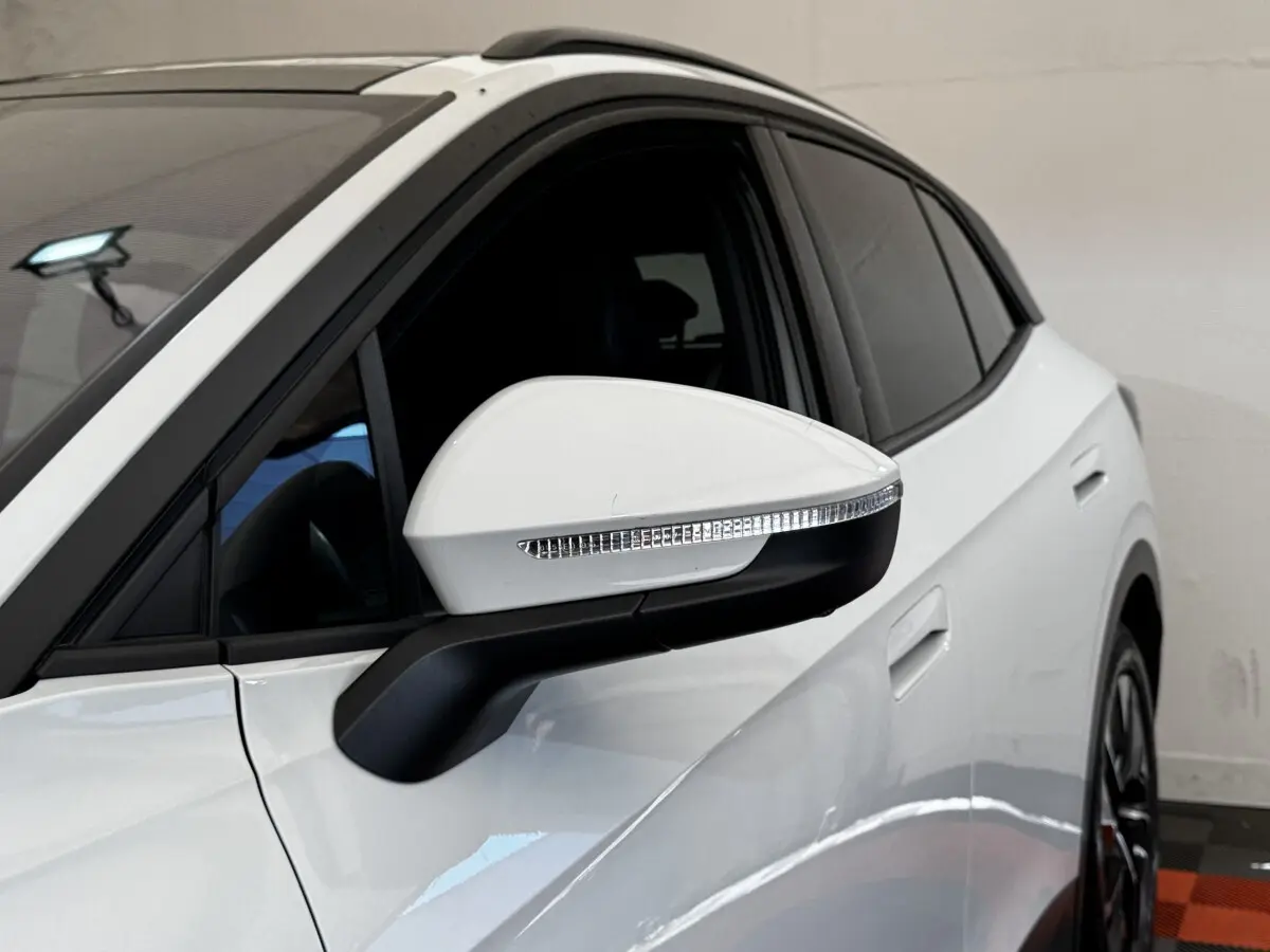 Vue latérale côté gauche d'un Volkswagen ID.4 blanc, mettant en valeur le rétroviseur rabattable avec clignotant intégré.