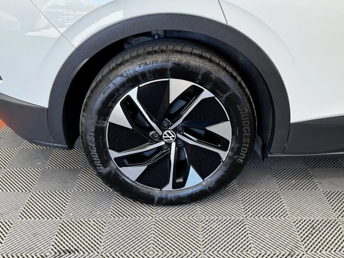 Gros plan sur la roue avant droite du Volkswagen ID.4 blanc, avec jante noire et argentée au design moderne.
