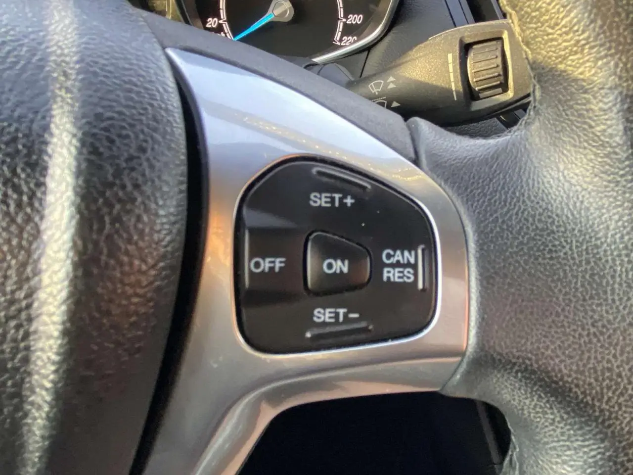 Gros plan sur les commandes du régulateur de vitesse au volant d'une Ford B-MAX blanche, tableau de bord en arrière-plan.