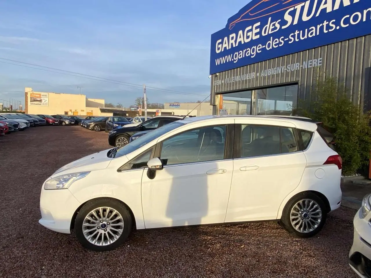 Ford B-MAX blanc en profil côté gauche, garé devant un garage avec jantes alliage 16 pouces visibles.