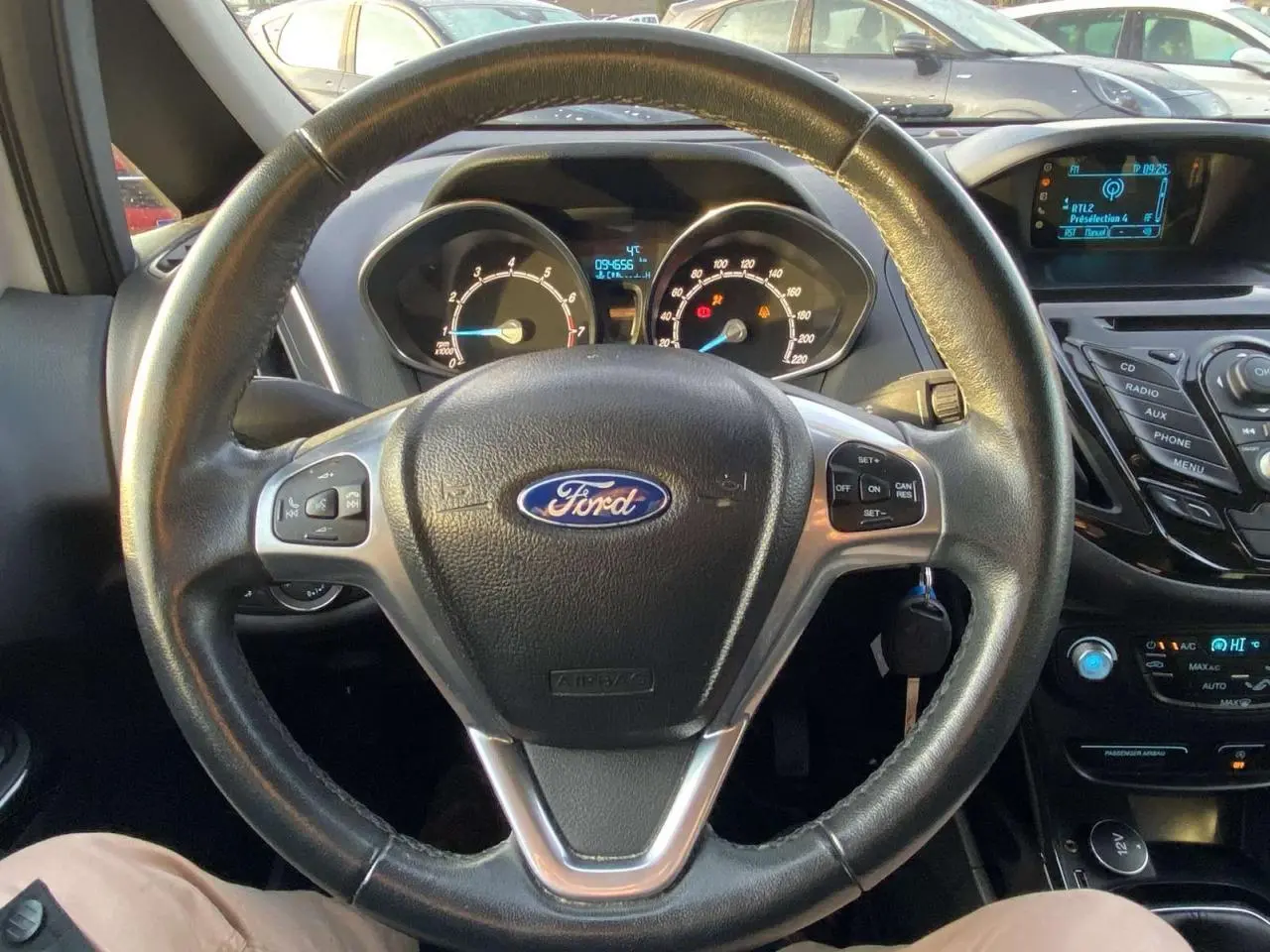 Vue intérieure centrée sur le volant cuir noir de la Ford B-MAX blanche, avec tableau de bord et commandes visibles.