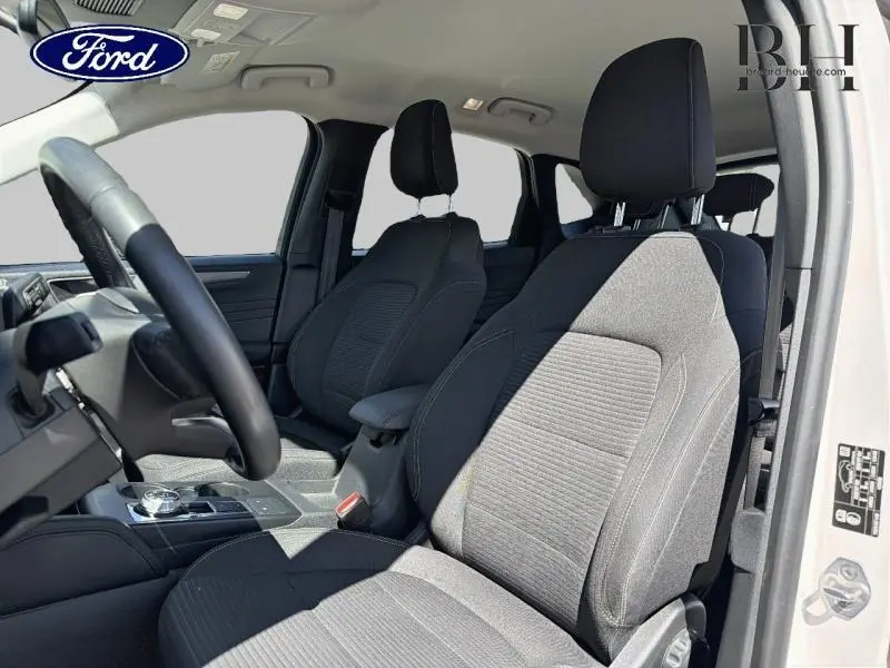 Vue intérieure côté conducteur du Ford Kuga 2023 blanc Glacier, sièges avant en tissu noir avec accoudoir central.