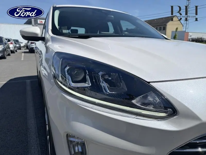 Gros plan sur le phare avant droit du Ford Kuga blanc glacier 2023, soulignant ses lignes modernes et LED.