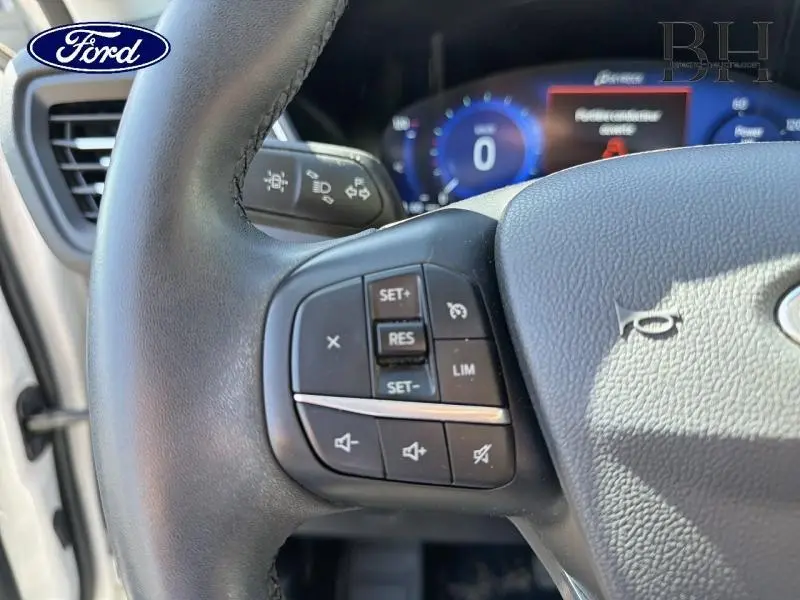 Gros plan sur le volant cuir multifonction côté gauche du Ford Kuga blanc Glacier avec commandes de régulateur et volume.