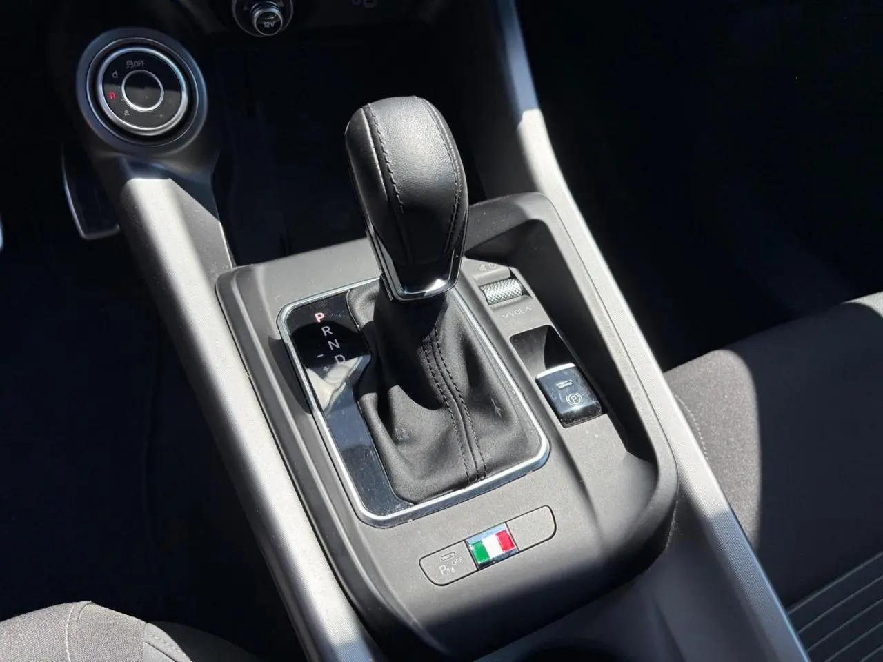 Gros plan sur la console centrale de l'Alfa Romeo Tonale blanche, avec levier de boîte auto et détail du drapeau italien.
