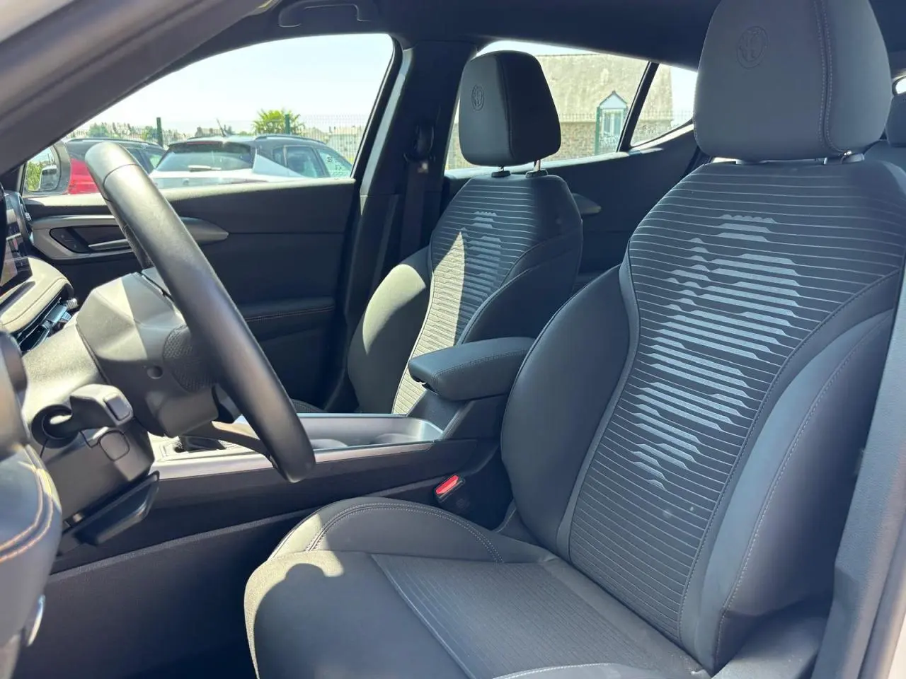 Vue intérieure côté conducteur de l'Alfa Romeo Tonale 2025, sièges noirs avec motif rayé et accoudoir central.