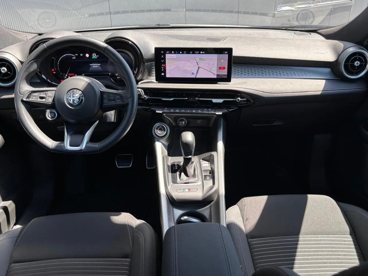 Vue intérieure avant de l'Alfa Romeo Tonale 2025 avec tableau de bord digital et volant sport en cuir noir.