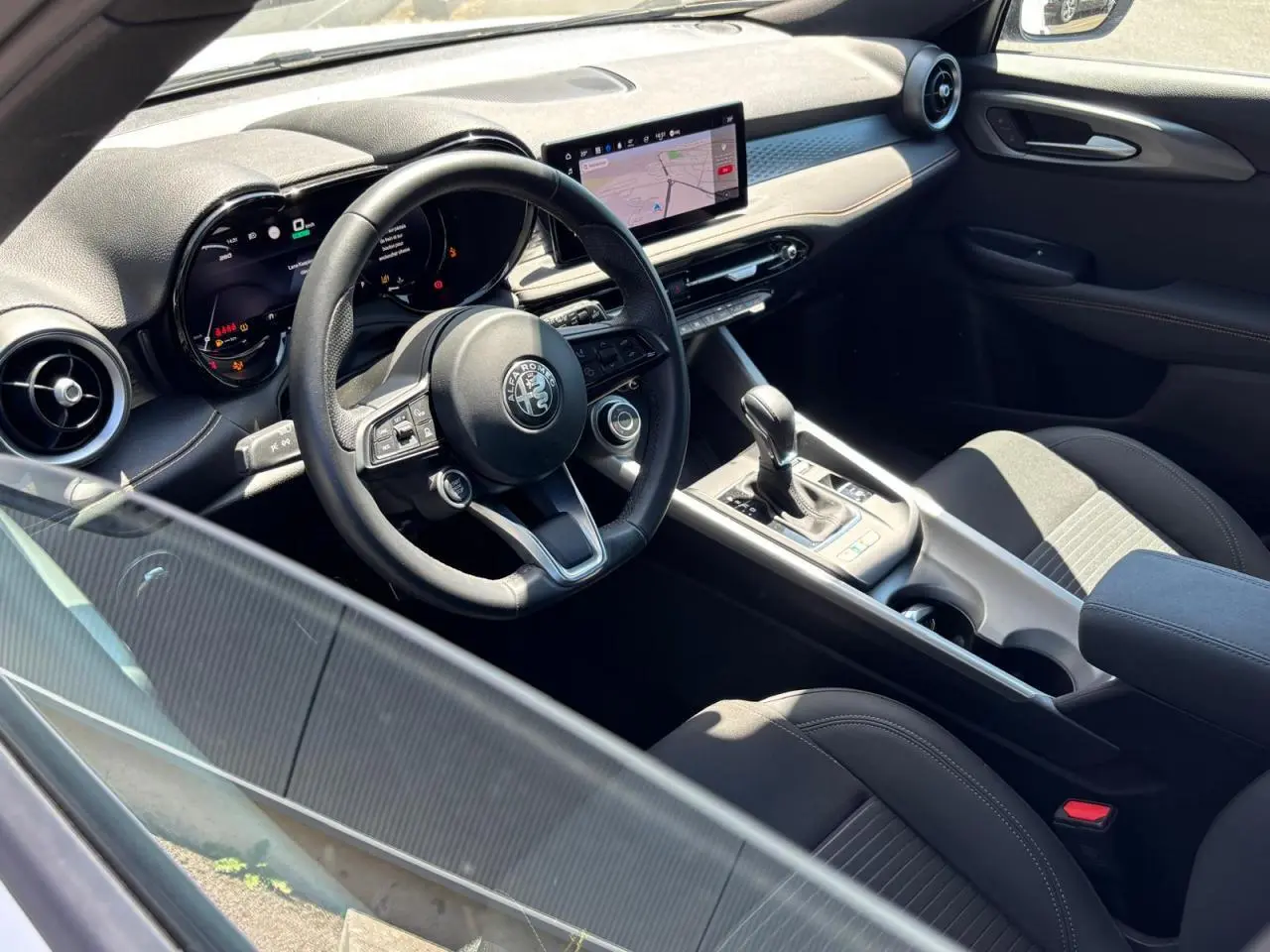 Vue intérieure côté conducteur de l'Alfa Romeo Tonale 2025, volant cuir, écran tactile et console centrale avec levier de vitesses.