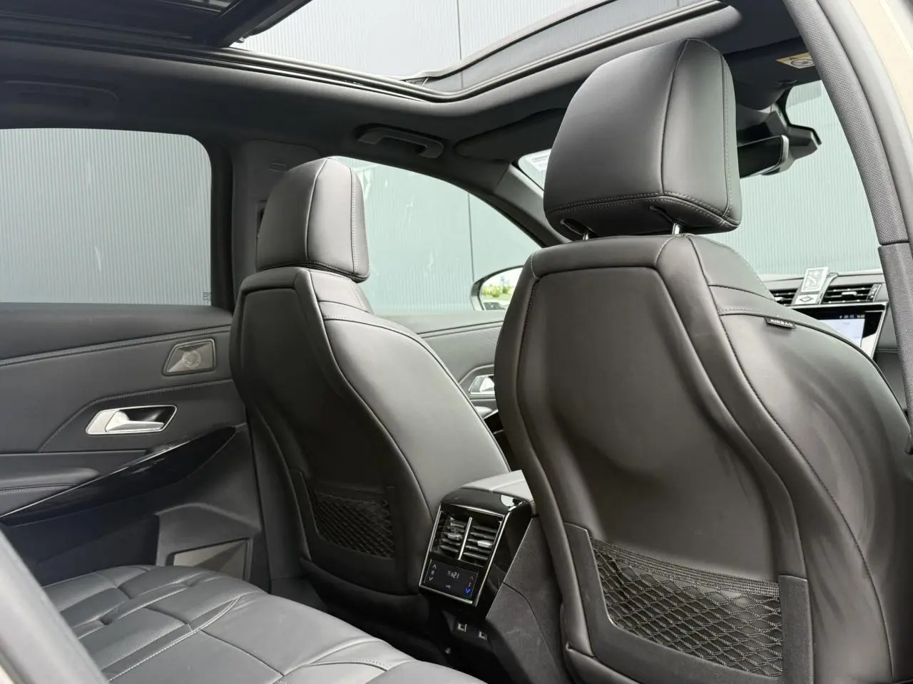 Vue intérieure arrière du DS7 2025 avec sièges en cuir noir Basalte et toit ouvrant panoramique ouvert.