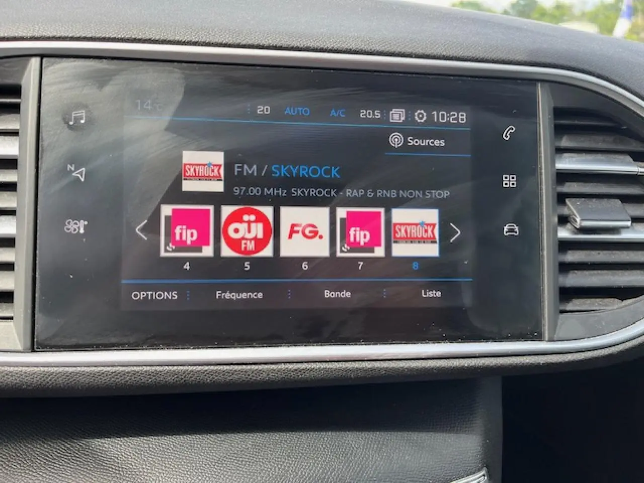 Écran tactile central de la Peugeot 308 gris clair affichant la radio FM sur Skyrock, avec commandes climatisation visibles.