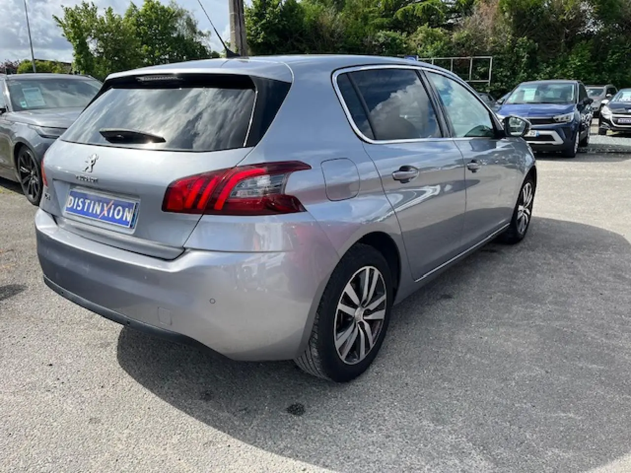 Peugeot 308 gris clair vue 3/4 arrière droit, avec feux arrière distinctifs et jantes alliage bicolores.