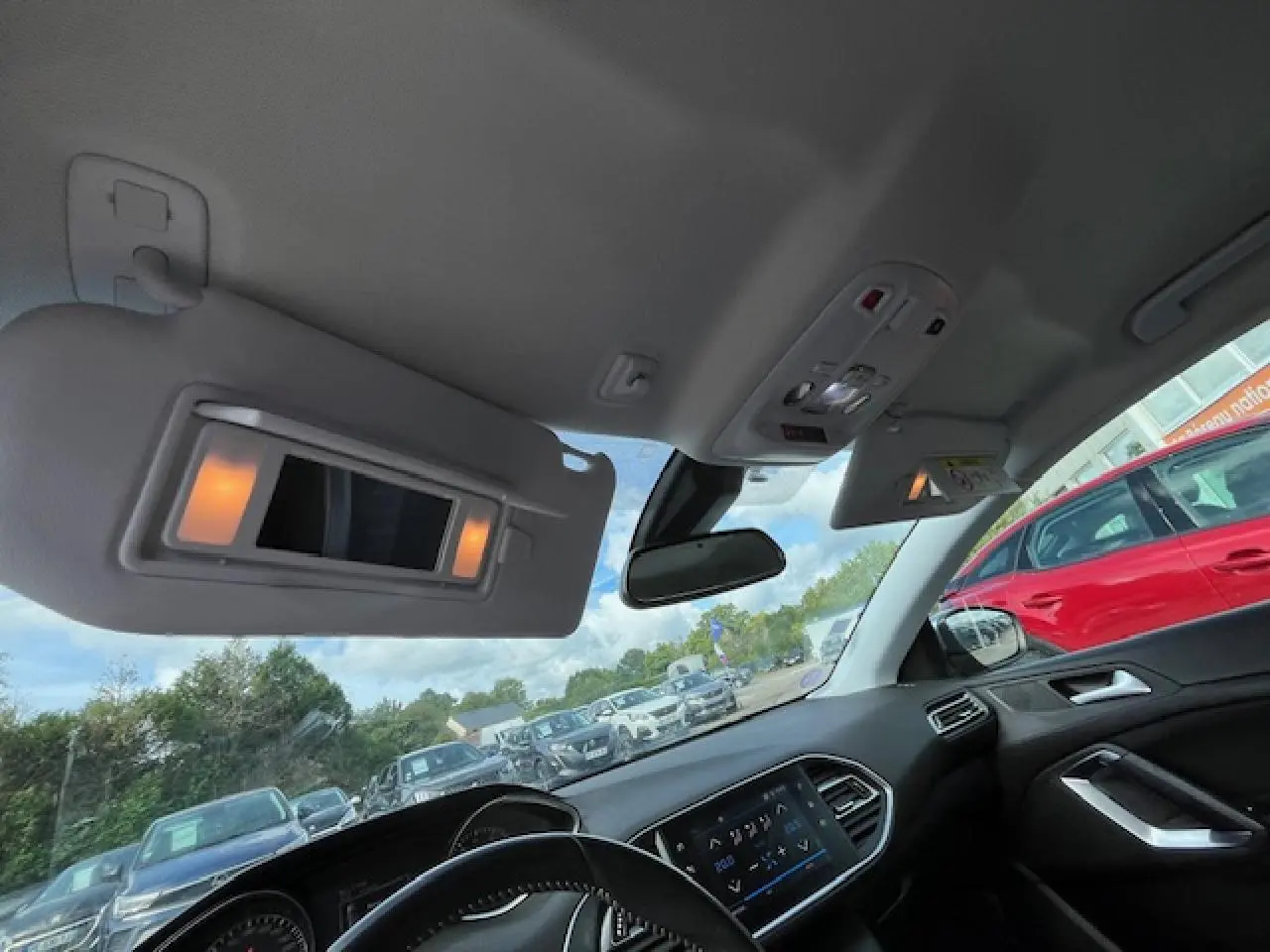 Vue intérieure avant de la Peugeot 308 gris clair, avec pare-soleil allumé et tableau de bord moderne visible.