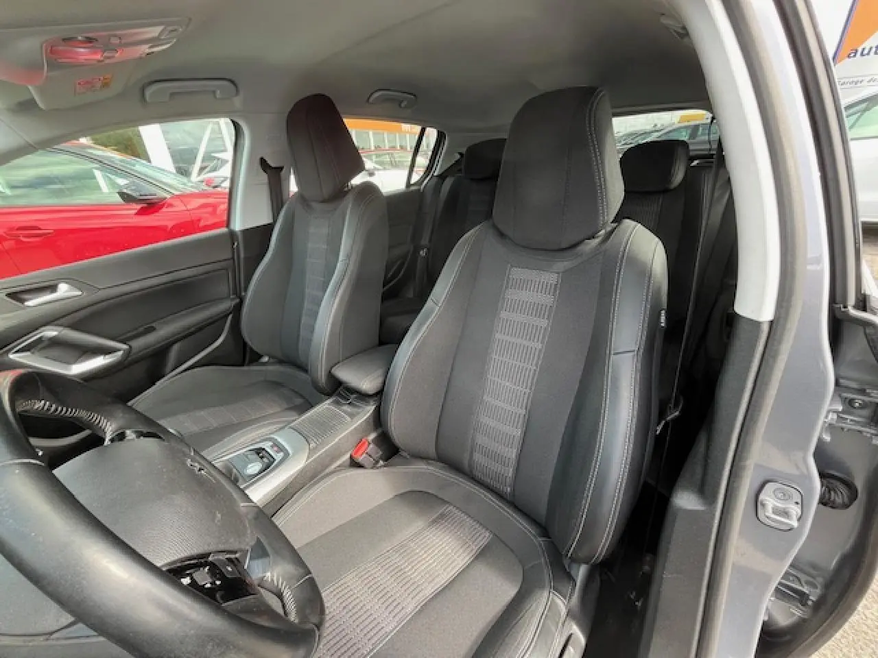 Vue intérieure côté droit montrant les sièges avant noirs et gris d'une Peugeot 308 gris clair de 2018 avec accoudoir central.