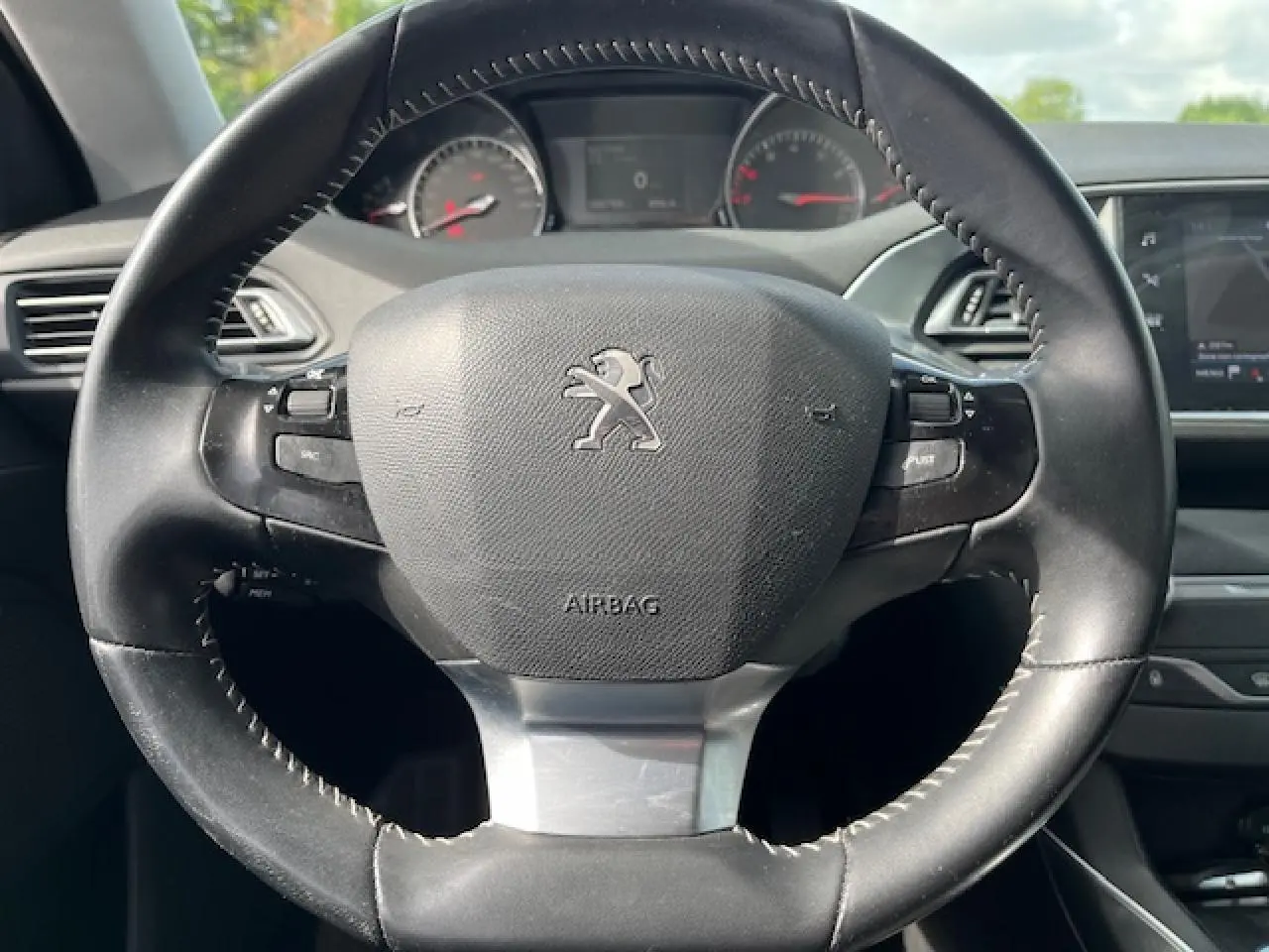Vue rapprochée du volant noir de la Peugeot 308 gris clair, avec tableau de bord et écran tactile en arrière-plan.