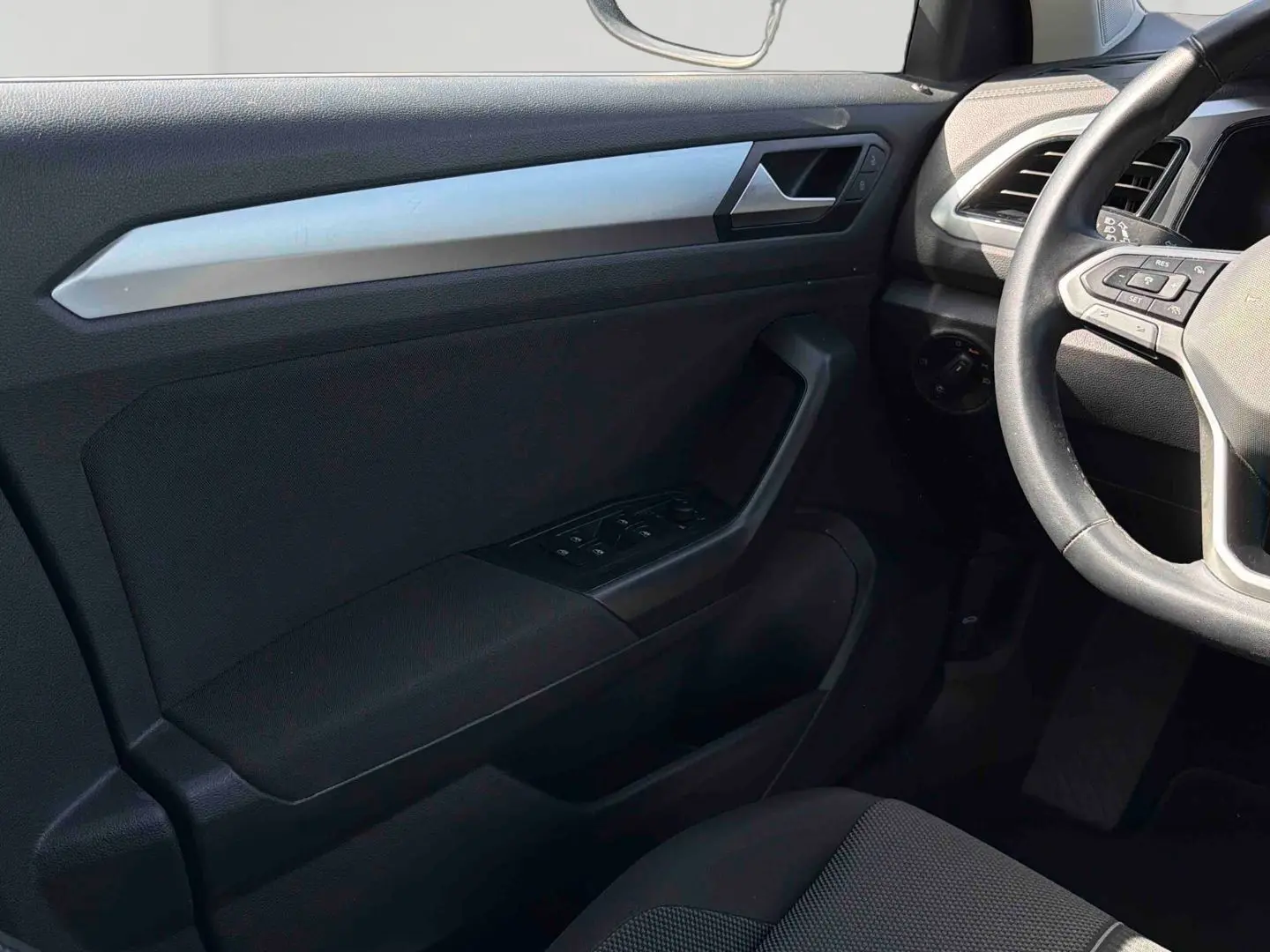Vue intérieure côté conducteur du Volkswagen T-Roc 2025, montrant la porte noire avec commandes des vitres et volant cuir multifonctions.