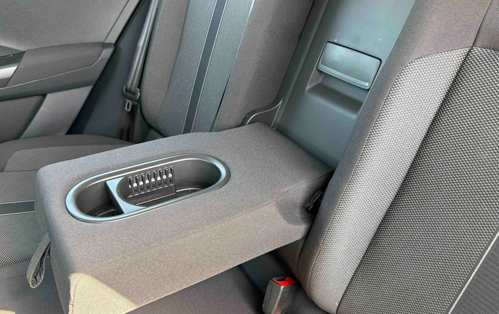 Vue rapprochée de l'accoudoir arrière avec porte-gobelets du Volkswagen T-Roc noir, intérieur tissu gris.