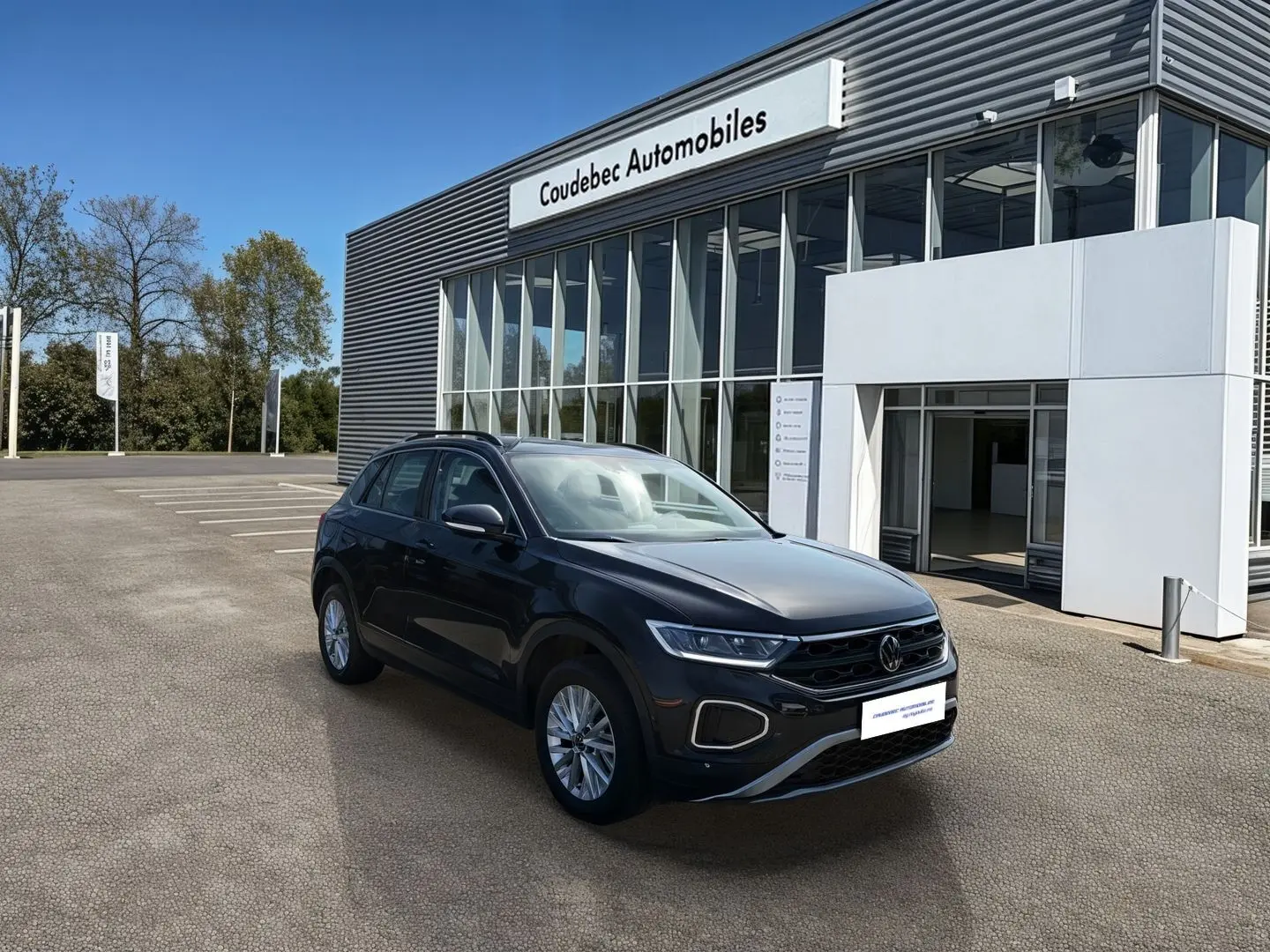 Volkswagen T-Roc noir vue 3/4 avant droit devant un bâtiment moderne de concession automobile.