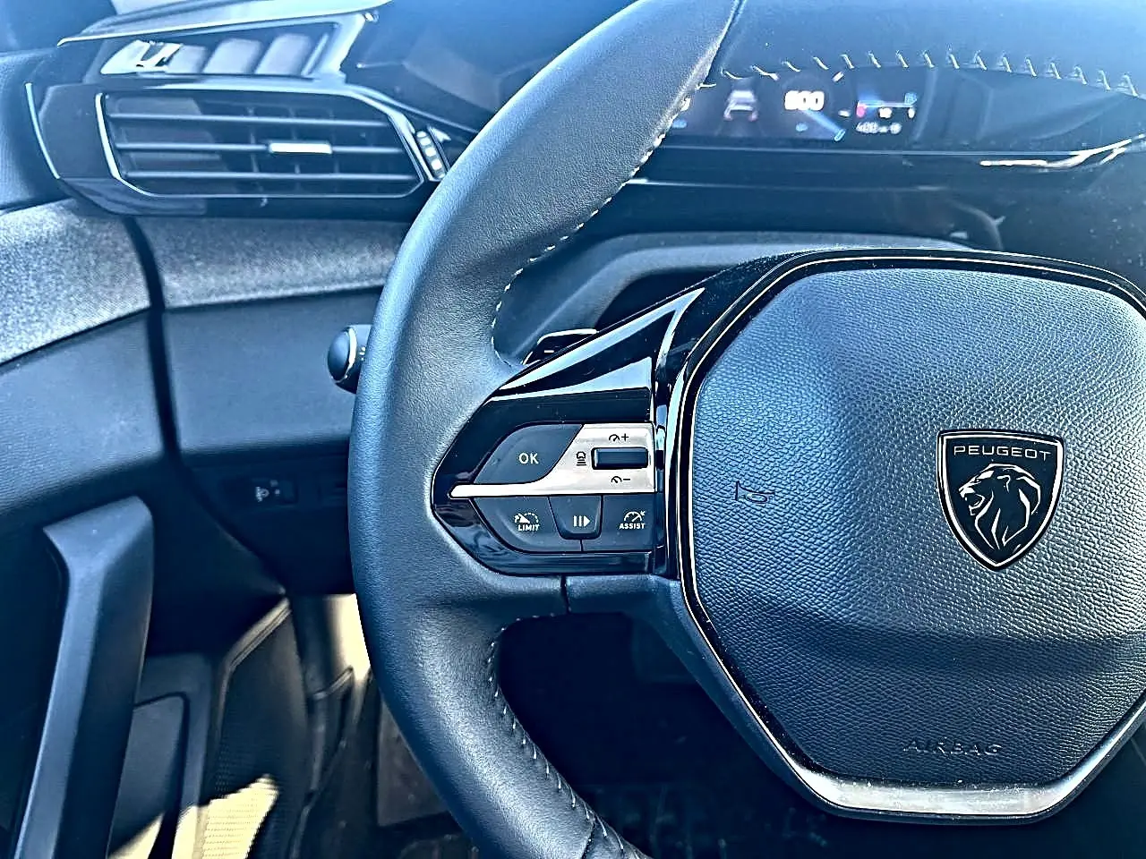 Vue rapprochée du volant multifonction noir de la Peugeot 308 gris selenium, avec tableau de bord numérique en arrière-plan.