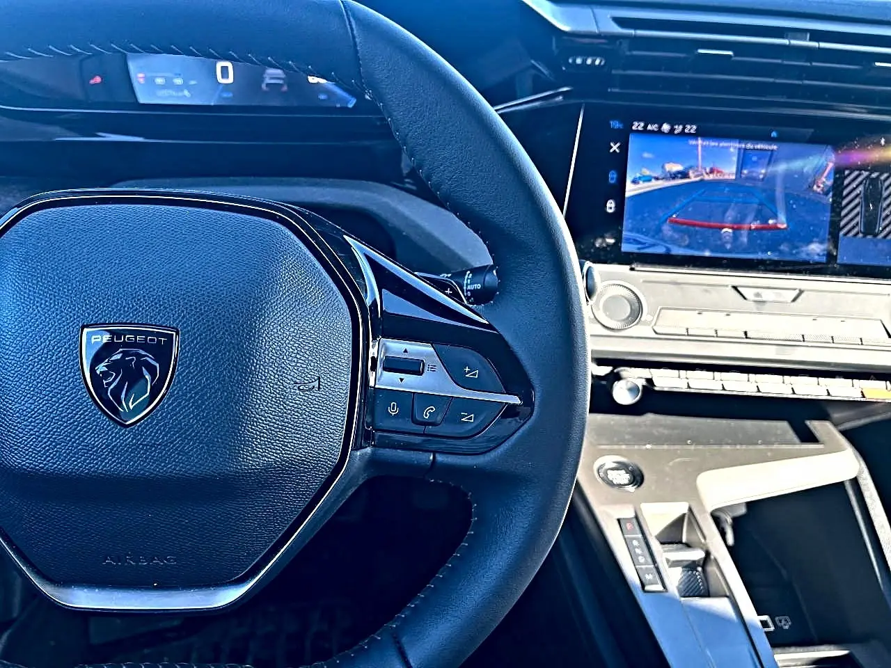 Vue rapprochée du volant multifonction noir et du tableau de bord digital avec écran tactile affichant la caméra de recul d’une Peugeot 308.