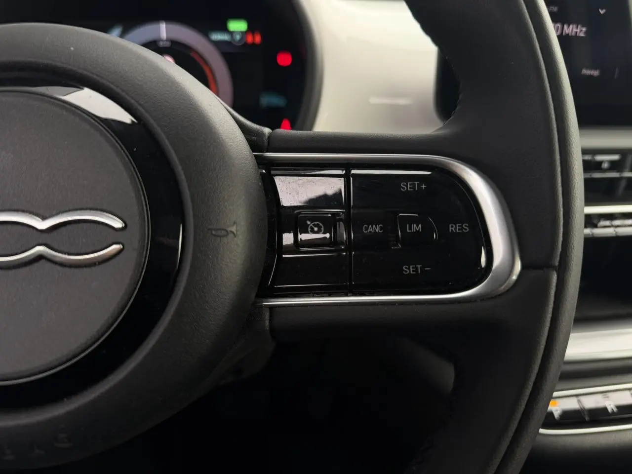 Gros plan sur le volant noir de la Fiat 500 électrique 2024, avec commandes du régulateur de vitesse visibles à droite.