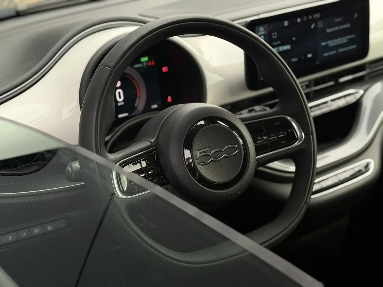 Vue intérieure rapprochée du volant noir et du tableau de bord blanc brillant de la Fiat 500 électrique 2024.