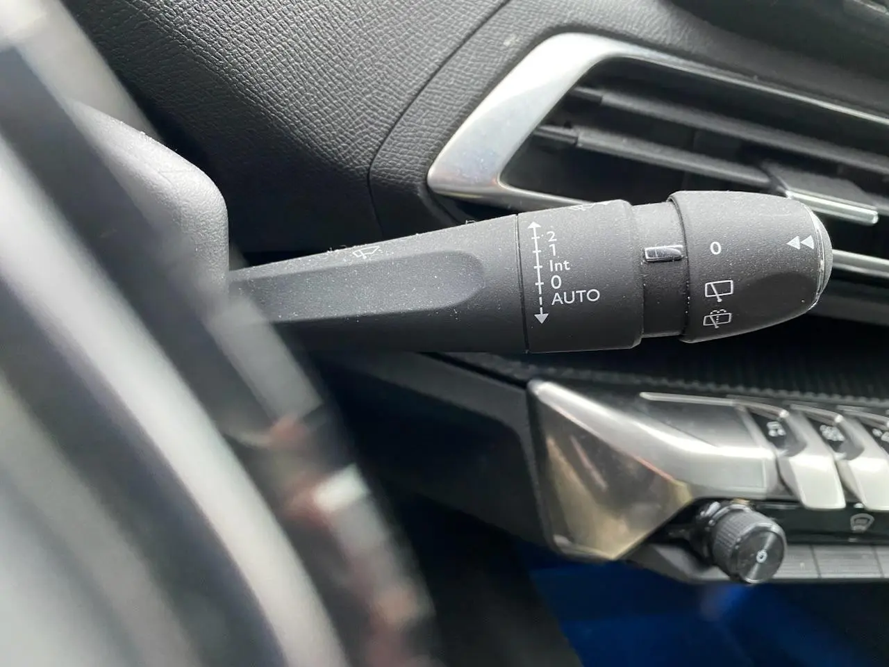 Gros plan sur la commande des essuie-glaces à gauche du volant dans l'habitacle noir du Peugeot 3008 gris platinium.