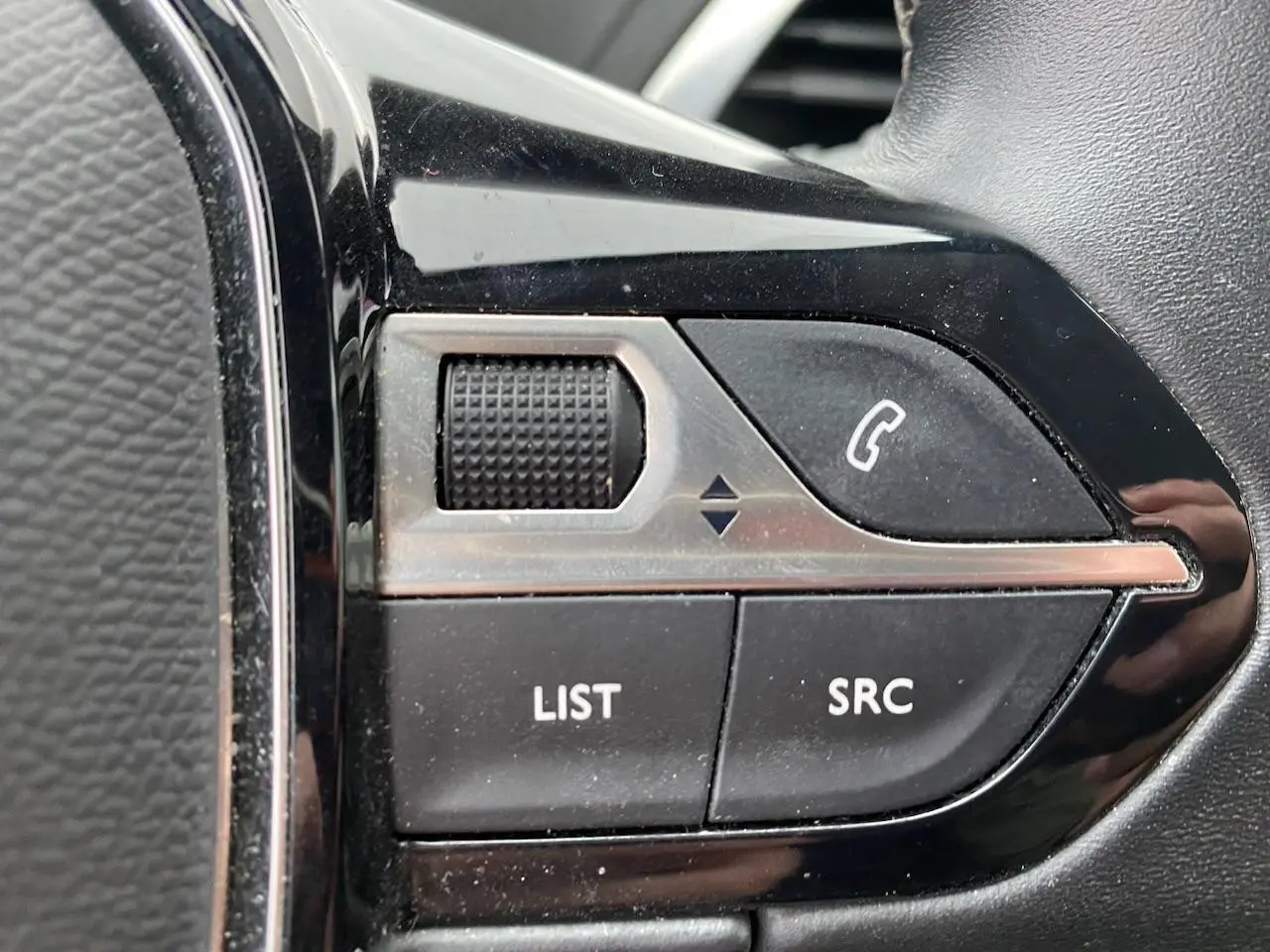 Gros plan sur les commandes du volant noir du Peugeot 3008 gris platinium, boutons pour téléphone et liste audio.