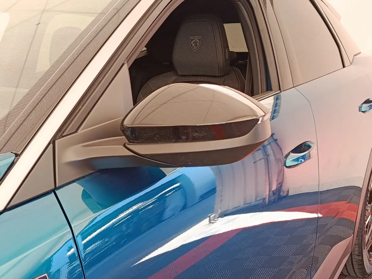 Vue rapprochée du rétroviseur côté gauche d’un Peugeot 3008 bleu 2025 avec siège avant et logo Peugeot visible.