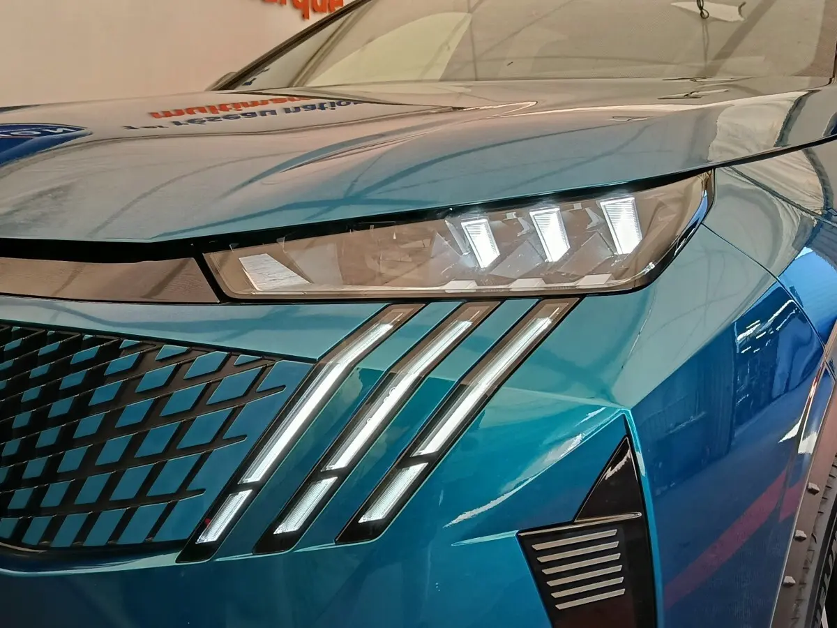 Gros plan sur le phare avant droit et la calandre bleue du Peugeot 3008 1.2 Hybrid 136 GT 2025.