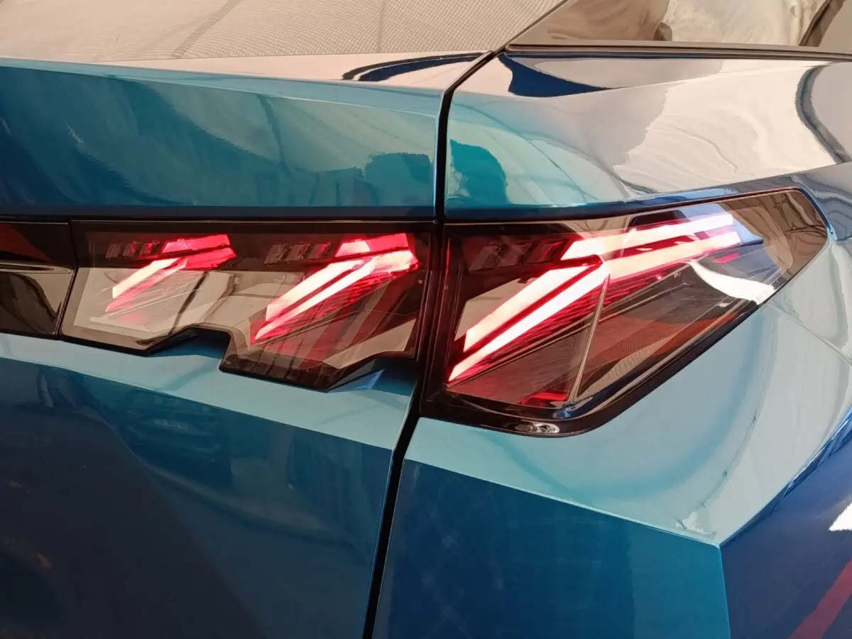Gros plan sur les feux arrière allumés du Peugeot 3008 bleu, soulignant les lignes anguleuses et modernes du coffre.