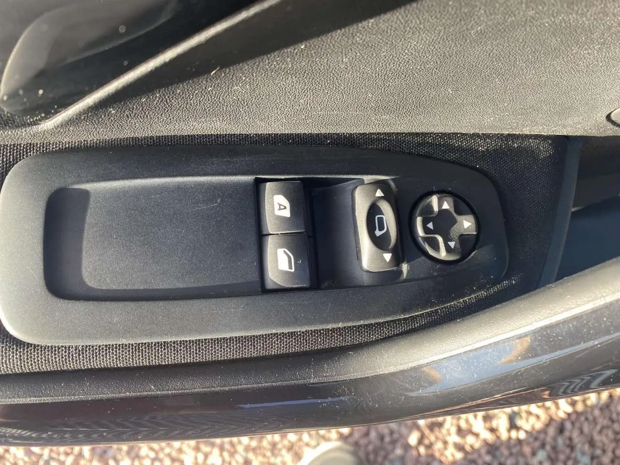 Gros plan sur les commandes de réglage des rétroviseurs et des vitres côté conducteur d’une Peugeot 208 noire de 2016.
