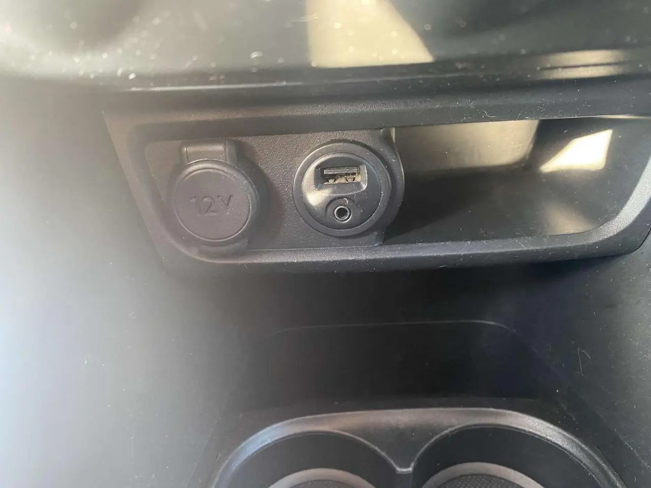 Prise 12V et port USB avec prise jack dans l'habitacle d'une Peugeot 208 noire, vue rapprochée du compartiment central.