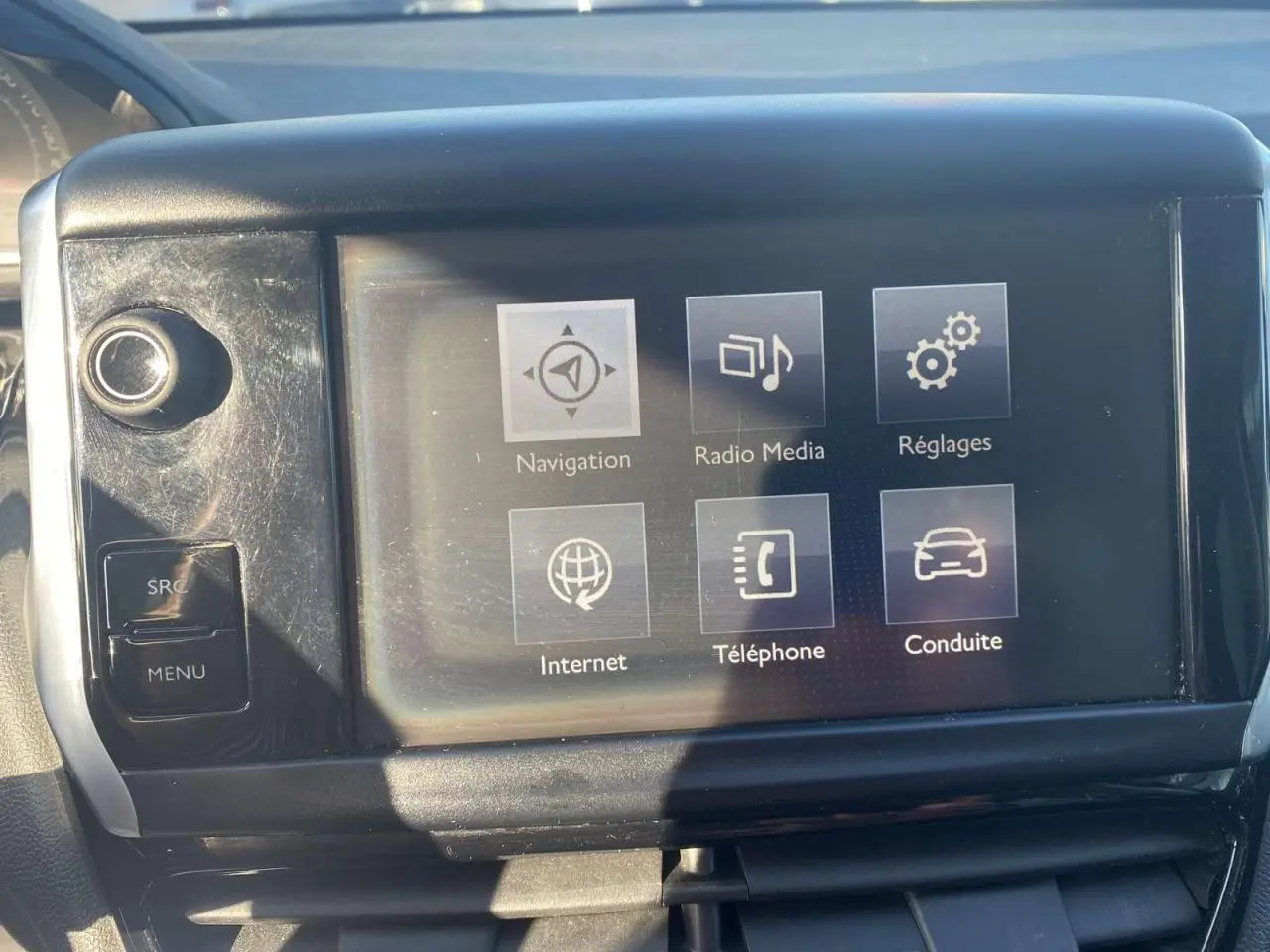 Écran tactile central de la Peugeot 208 noir, affichant les options navigation, radio, réglages et téléphone.