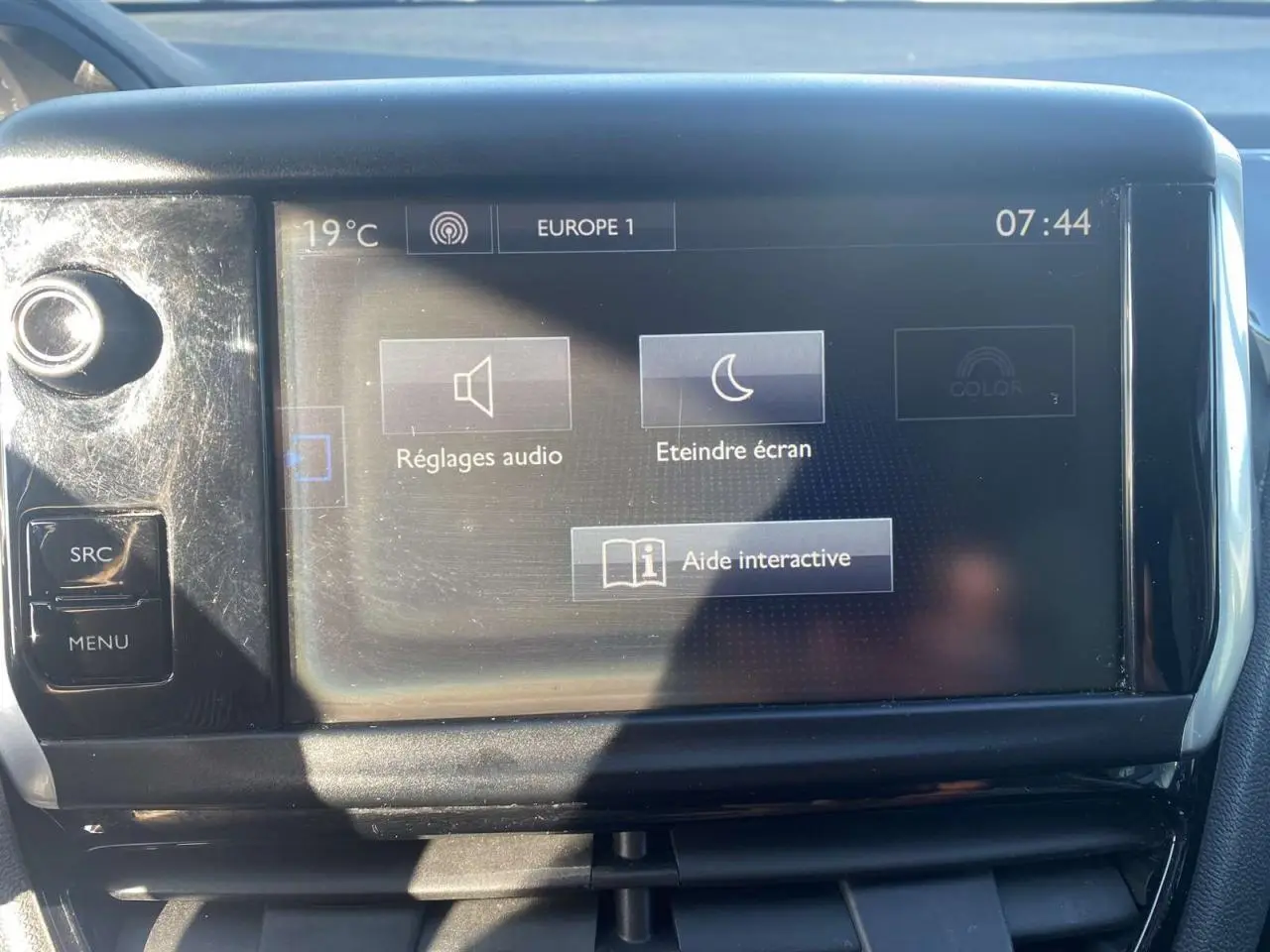 Écran tactile central de la Peugeot 208 noir, vue frontale, affichant les réglages audio et aide interactive.