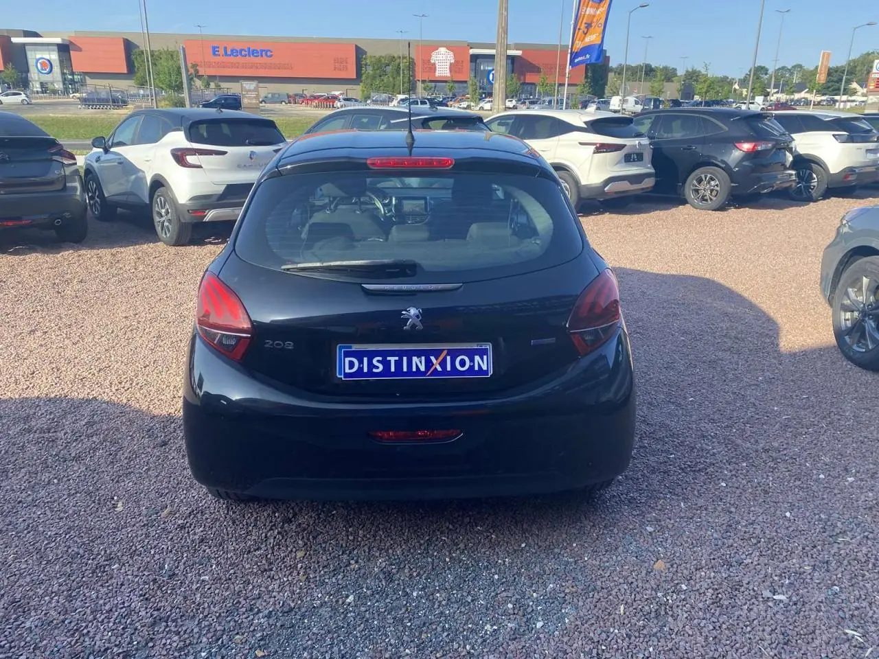 Vue arrière d'une Peugeot 208 noire 2016 avec plaque Distinxion, stationnée sur un parking en gravier.