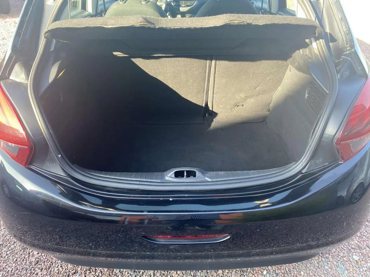 Coffre ouvert vu de l'arrière d'une Peugeot 208 noire, montrant l'espace de chargement vide et la peinture métallisée.