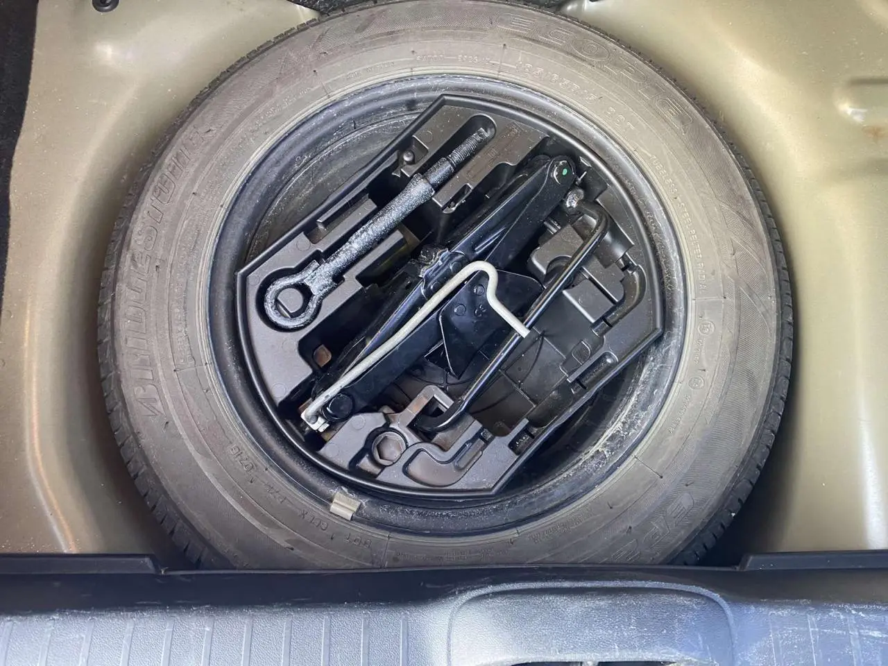 Gros plan sur la roue de secours acier 15 pouces et les outils de bord du coffre d'une Peugeot 208 noire.