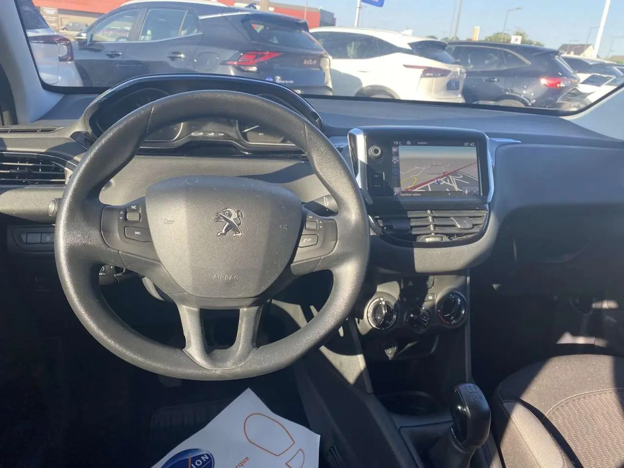Vue intérieure centrée sur le volant Peugeot et l'écran tactile GPS, avec tableau de bord et levier de vitesse visibles.