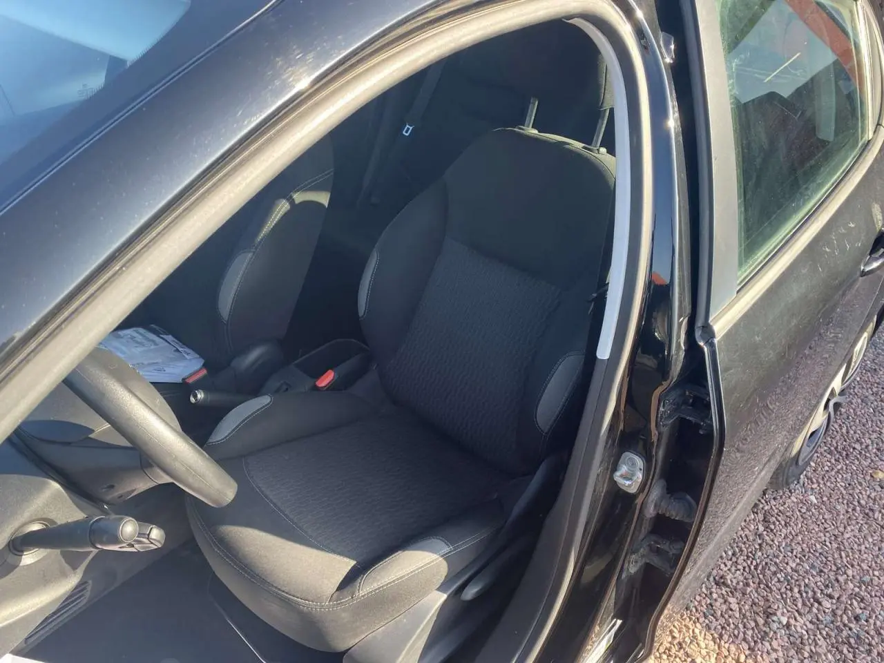 Vue intérieure côté conducteur d'une Peugeot 208 noire de 2016, montrant le siège avant et le volant multifonction.