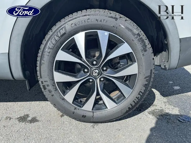 Gros plan sur la roue avant droite d'un Renault Arkana blanc perle avec jante alliage noire et argentée.