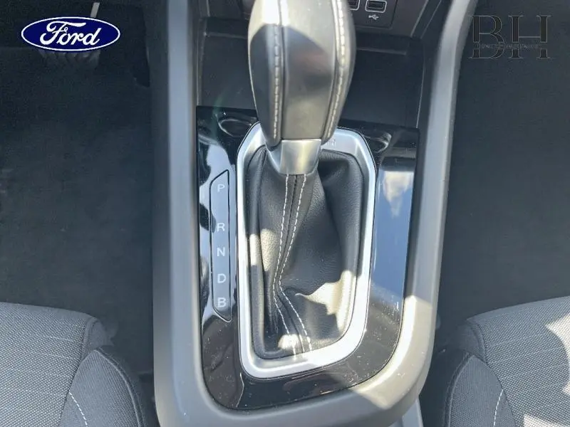 Le levier de vitesses automatique noir vu de dessus avec coutures blanches, entouré de plastique brillant.