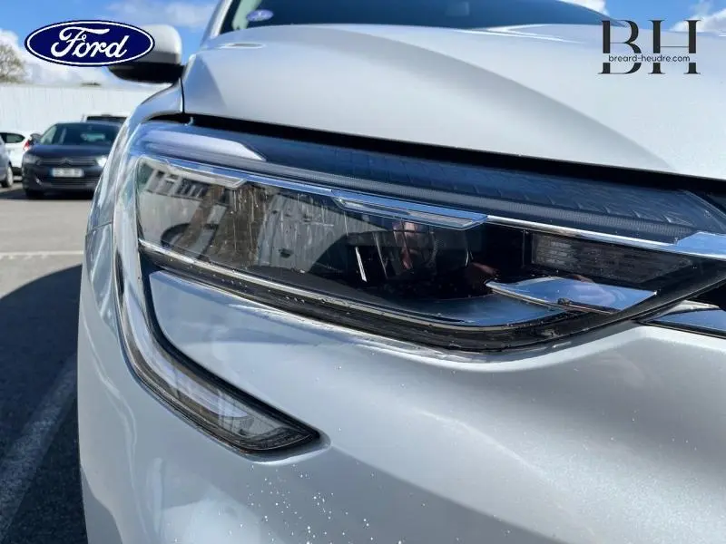 Gros plan sur le phare avant droit d'une Renault Arkana blanc perle, soulignant ses lignes modernes et son éclairage LED.