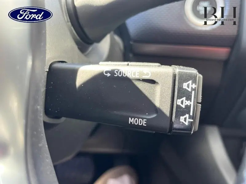 Gros plan sur la commande au volant noir du Renault Arkana blanc perle, avec boutons source et mode visibles.