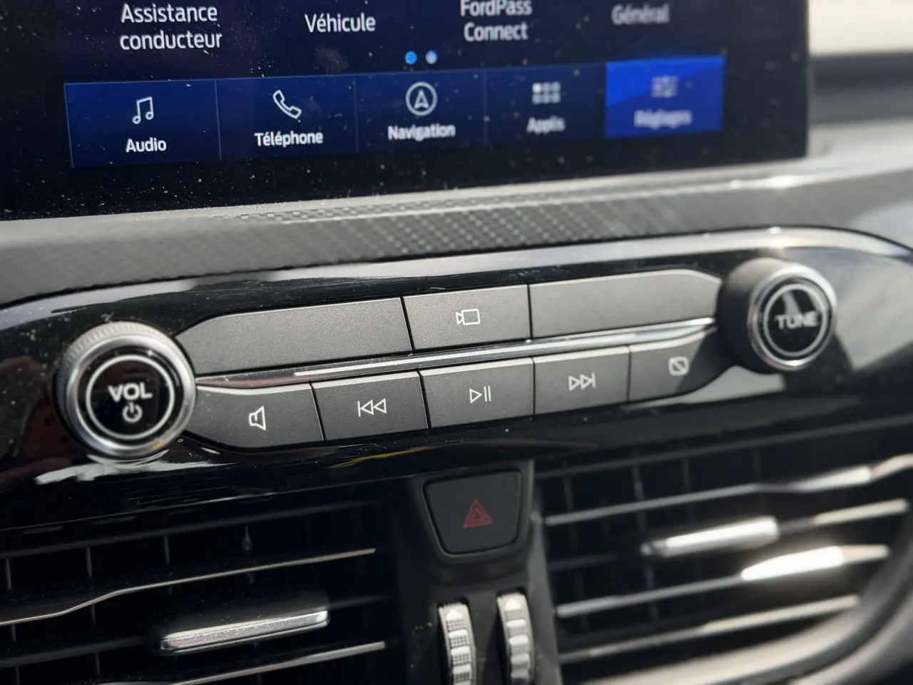 Gros plan sur la console centrale noire du Ford Kuga gris Solar 2023 avec commandes audio et écran tactile partiel visible.