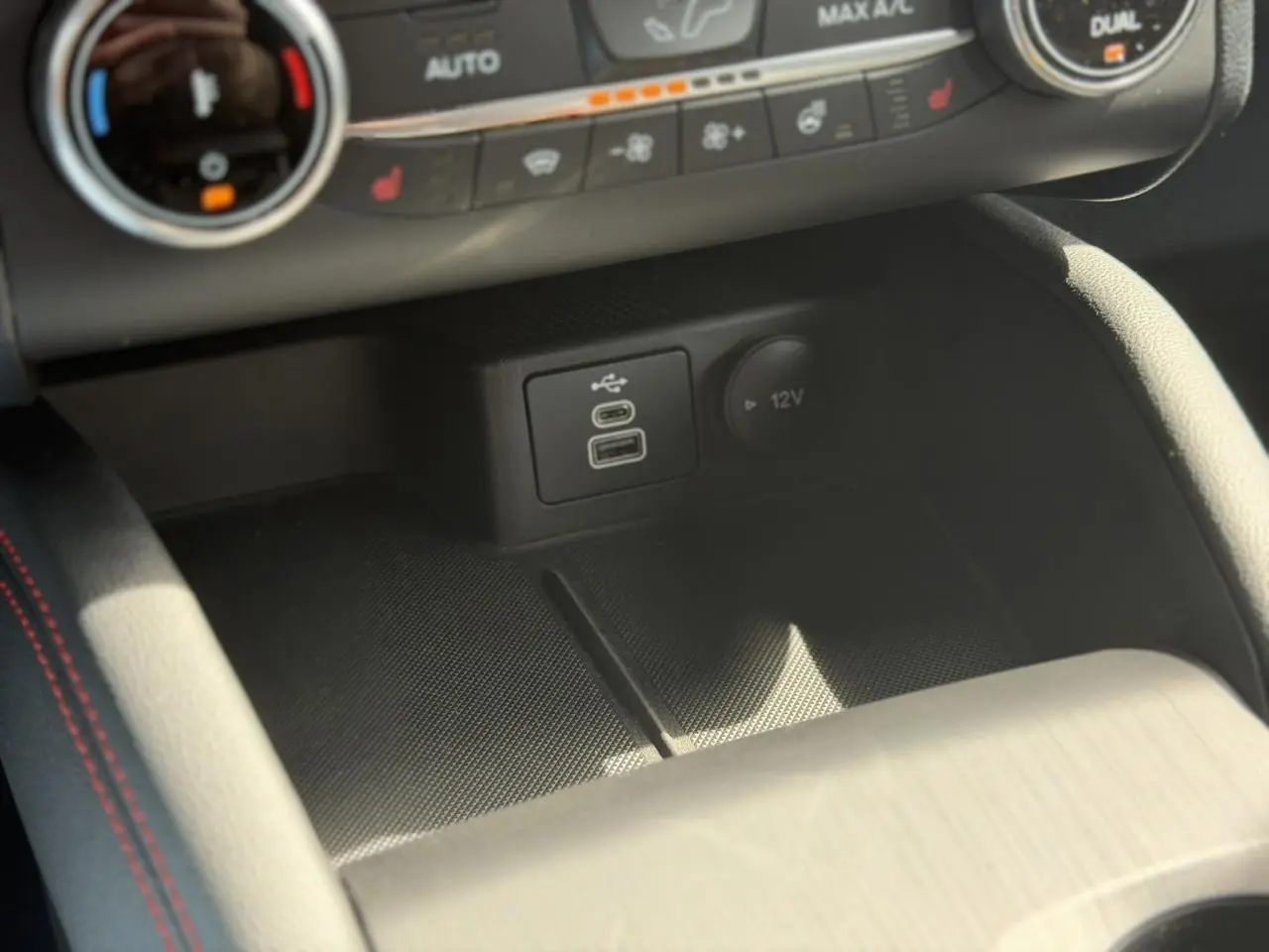 Gros plan sur la console centrale du Ford Kuga gris Solar, montrant les ports USB et la prise 12V avec surpiqûres rouges.