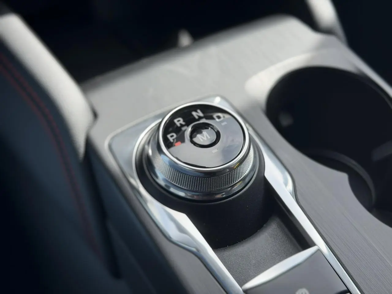 Gros plan sur le sélecteur rotatif de la boîte automatique du Ford Kuga gris Solar, avec console centrale et porte-gobelets.