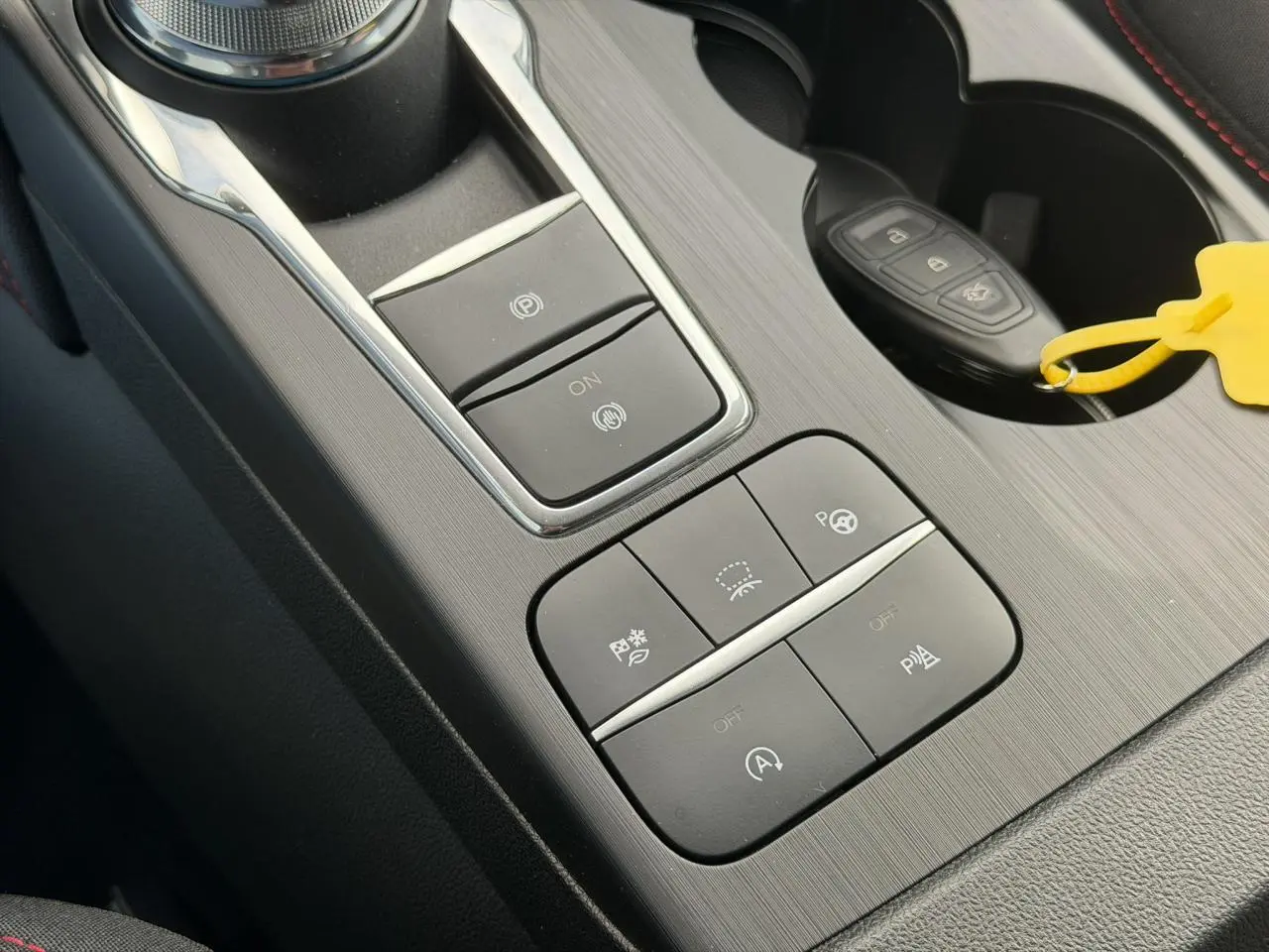 Gros plan sur la console centrale du Ford Kuga gris Solar 2023, avec boutons de contrôle et clé dans porte-gobelet.